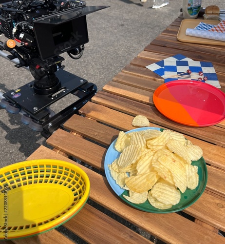 Outdoor Film Set Snack Table With Potato Chips, Colorful Plates and Camera Equipment