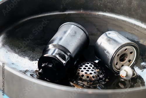 Used oil filter and drain plug sitting in an oil drain pan after an oil change