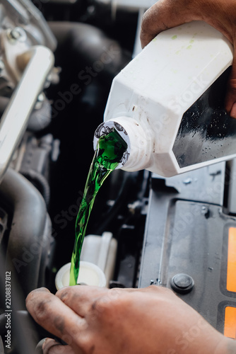 Mechanic adding green antifreeze liquid to a car engine during maintenance