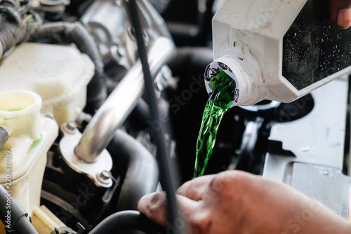 Mechanic adding green antifreeze liquid to a car engine during maintenance
