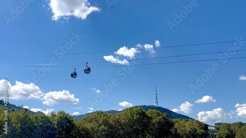 Two cable cars traveling above a green landscape beneath a blue sky. Tourism scene illustrating mountain transportation, sightseeing, leisure and scenic travel.