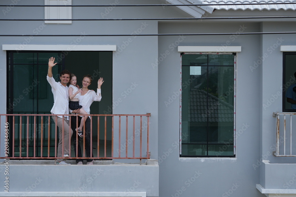 Obraz premium Caucasian family of three embracing greet the neighborhood from the balcony with their daughter on the balcony of their new house overlooking the residential estate, shallow depth of field