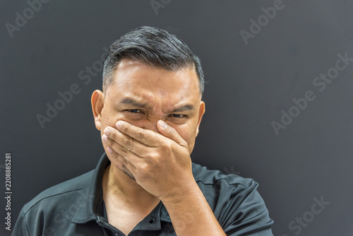 Fotografie A man covers his mouth one hand frowns against dark background expressing discom