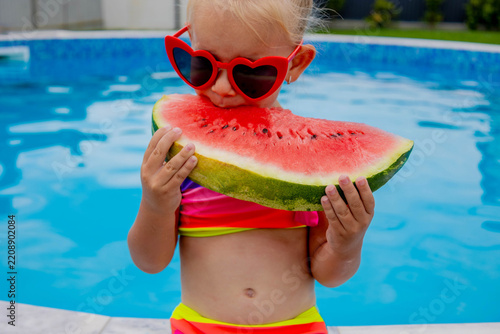 Girl in heart sunglasses eating watermelon slice near swimming pool in summer