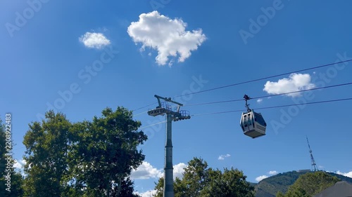 Cable car cabin traveling above trees beneath a blue sky. Scenic transport scene illustrating tourism, mountain travel, aerial transportation and leisure.