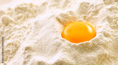Raw egg yolk sits in a mound of white flour for baking preparation