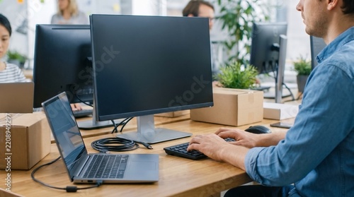 Male IT employee typing on keyboard configuring computer monitor and laptop workstation with cardboard boxes in modern corporate office   