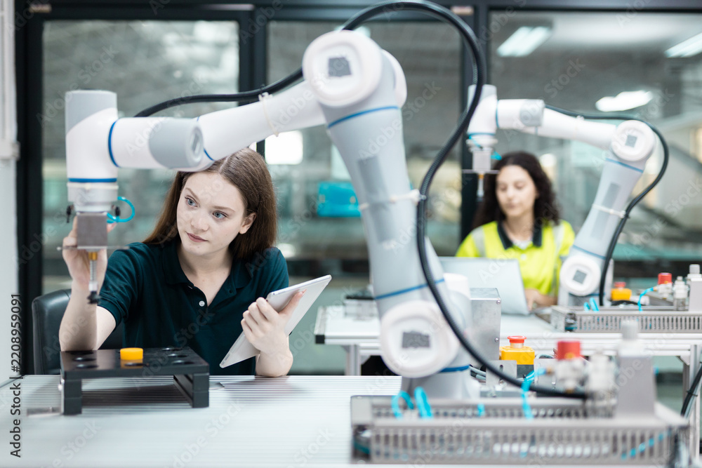 Obraz premium Engaged young woman student engineer in teamwork, learning about robot technology with robotic arm. Future education for industry automation and modern programming for machinery