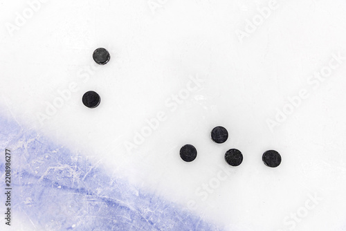Ice hockey pucks scattered on a scratched ice rink, top view of black pucks on frozen surface with copy space.