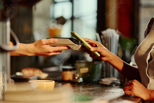 Close up of African American young woman making contactless payment with smartphone at POS terminal. Image suitable for mobile banking and fintech ads