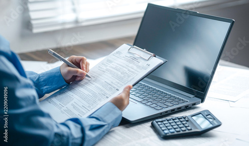 A professional accountant is taking notes on a clipboard regarding tax forms placed next to a laptop and a calculator, covering corporate tax filing, electronic tax filing, financial consulting servic