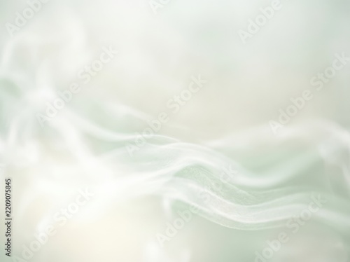 Wispy white smoke trails rising gently against a soft pastel green and cream background with subtle bokeh