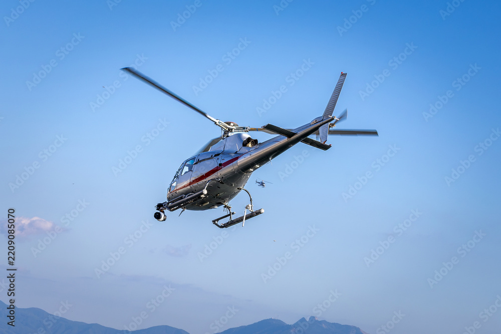 Fototapeta premium A TV broadcast helicopter equipped with camera gear hovering in the blue sky to record live aerial footage.