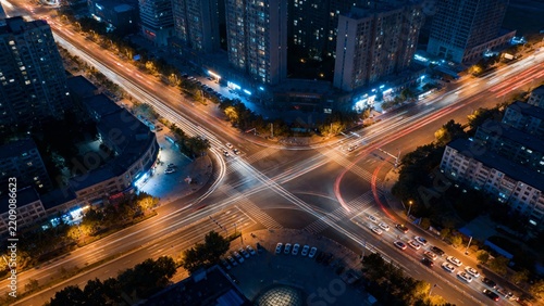 Nighttime aerial view of a busy urban intersection with light trails from moving vehicles
