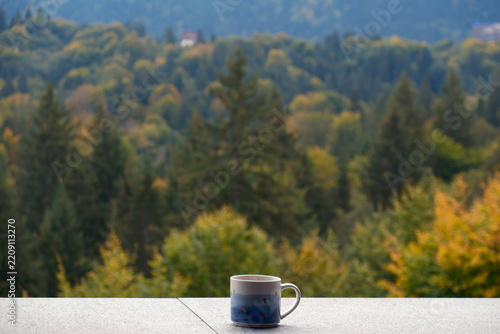 Fotografie A ceramic mug on a hotel balcony overlooking the beautiful autumn pine forests of Poiana Brasov resort in the Carpathian Mountains, Romania
