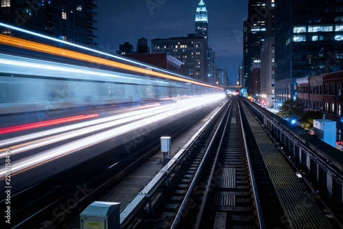 Nighttime cityscape with light trails from moving vehicles on an elevated railway track