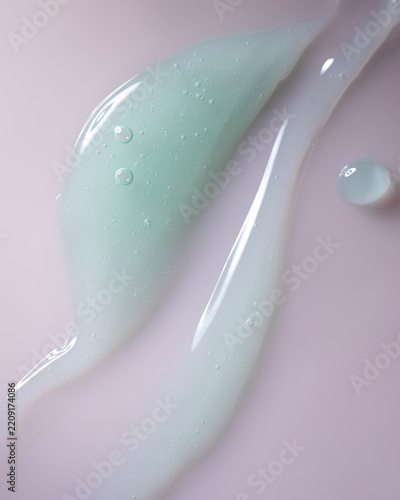 Fotografie Pale blue translucent gel forms two elongated smears and a rounded droplet on a soft pink background, with trapped air bubbles and glossy highlights creating an abstract texture