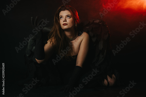 Fotografie A young woman wearing black feathered wings poses in a dramatic low-key portrait