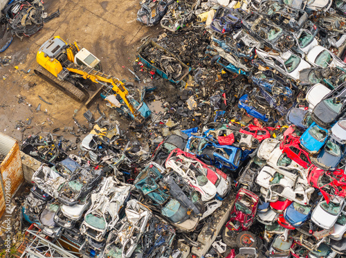 Aerial view of an end of life vehicle recycling facility with a yellow excavator sorting through a large pile of crushed and dismantled cars in Gdansk, Pomeranian Voivodeship, Poland.