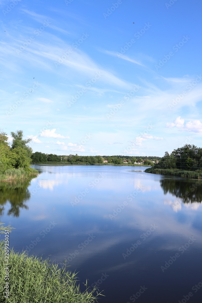 Obraz premium Clear water reflects cloudy sky over calm river near trees