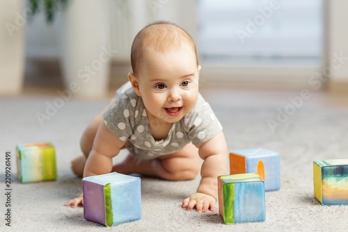 Happy baby crawling among colorful building blocks indoors