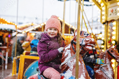 Adorable little girl riding merry-go-round carousel horse at Christmas funfair outdoors. Happy child enjoying traditional family Xmas market in Nuremberg, Germany
