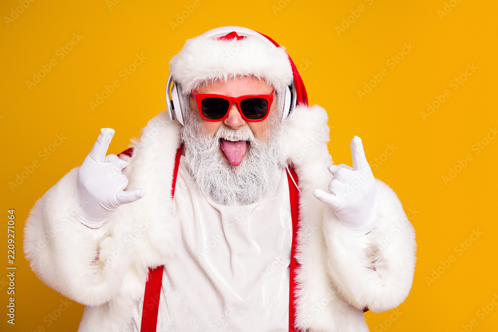 Obraz premium Cool Santa Claus wearing headphones and red sunglasses celebrating Christmas with playful rock gesture on bright yellow background