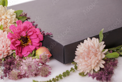 Horizontal close-up of black gift box with pink, peach and cream flowers on white background, elegant floral celebration composition for birthday, wedding, anniversary, greeting card and romantic