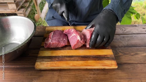 Close-up of a person in black gloves slicing meat on a wooden table outdoors. High quality 4k footage