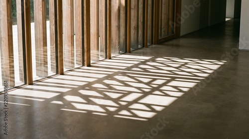 Geometric shadows cast by sunlight through window blinds onto a concrete floor inside a modern building.