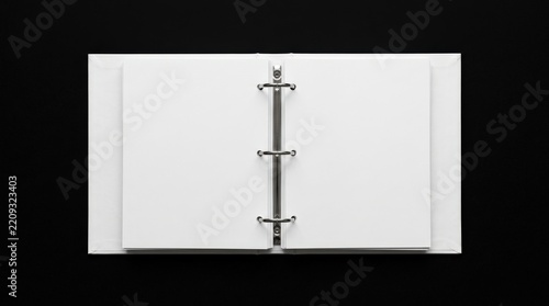 Blank white ring-binder notebook opened against a deep black background, minimalist stationery mockup photography, metal rings sharply defined, centered high-contrast composition, clean empty pages,