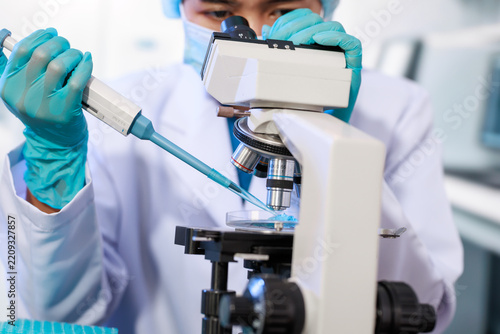Close-up of a laboratory scientist in gloves using a pipette beside a microscope, preparing a slide for medical research and testing.