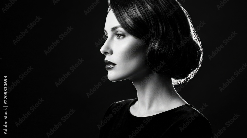 Fototapeta premium Elegant woman shown in sharp black-and-white side profile against a deep black background, fine-art beauty photography, sculpted cheekbone and glossy lips, dramatic rim lighting, high contrast,