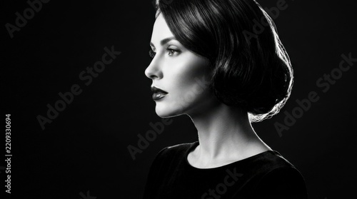 Elegant woman shown in sharp black-and-white side profile against a deep black background, fine-art beauty photography, sculpted cheekbone and glossy lips, dramatic rim lighting, high contrast,