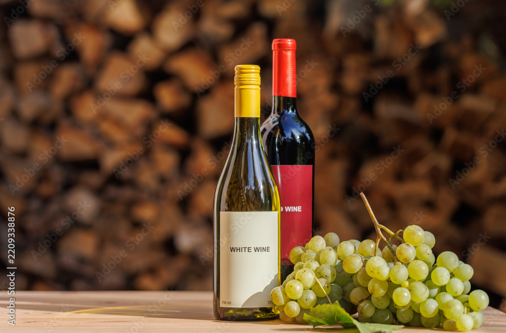 Obraz premium Wine Bottles and Green Grapes Against Stacked Firewood