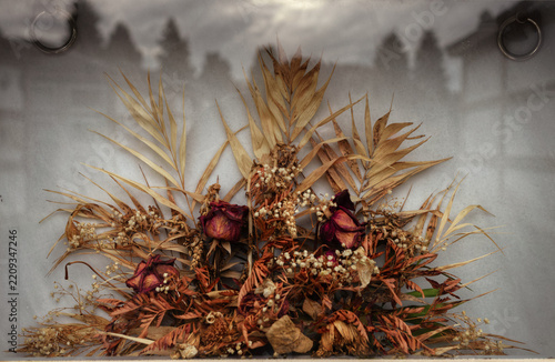 A bouquet of dried flowers behind a pane of glass that reflects other niches
