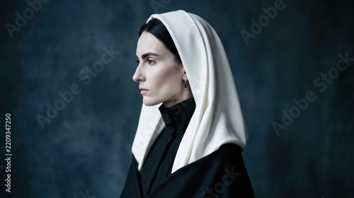 Pale woman in profile wearing a white hood or veil over a black high-neck garment, avant-garde fashion portrait, deep blue-gray background, cool soft light, sharp cheekbones and austere futuristic