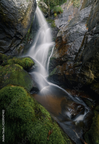 A waterfall cascades over granite rocks turning the surrounding moss a vibrant green