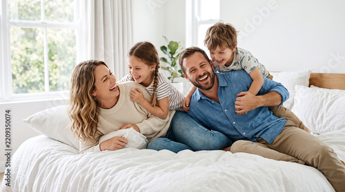 Joyful parents and kids laughing together on a comfortable bed perfect for happy childhood memories and strong family relationship concepts