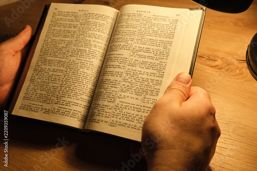 Person hold open book on wooden table under warm light for study session