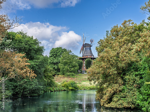 Traditional windmill standing beside serene riverbank with lush greenery, Bremen, Germany