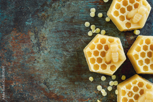 Honeycomb and bee shaped yellow beeswax blocks with wax pellets on rustic wooden  background.