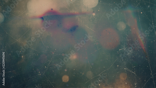 vintage damaged film texture with faded pastel bokeh, heavy scratches, dust specks, rainbow light leak and worn grunge surface on muted teal green background for overlays and designs