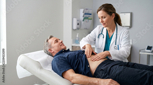 Female doctor examining patient abdomen, professional physician feeling stomach of man with focus and concern in clinic office setting