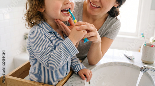 Mother helping child brush teeth happy smiling morning routine in bathroom with healthy hygiene habit to ensure clean bright white tooth