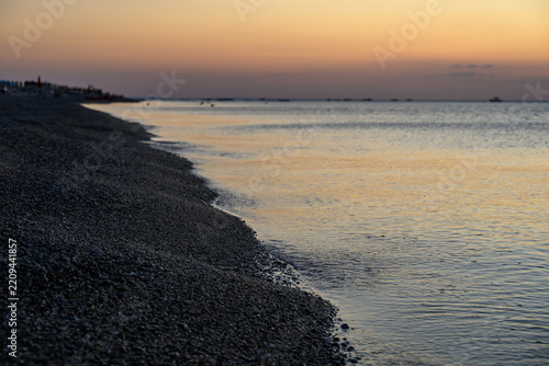 Tranquil coastal shoreline with gentle ocean waves hitting the pebble beach at twilight.