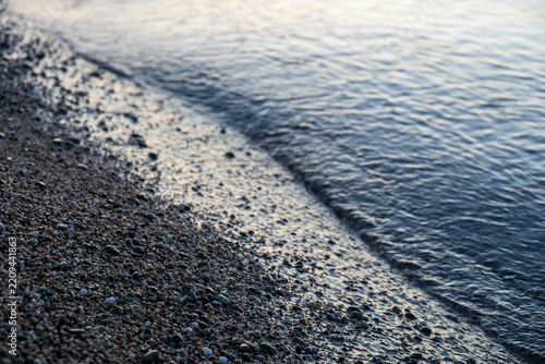 Tranquil coastal shoreline with gentle ocean waves hitting the pebble beach at twilight.