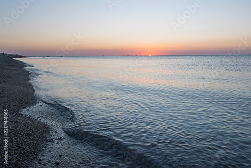 Tranquil coastal shoreline with gentle ocean waves hitting the pebble beach at twilight.