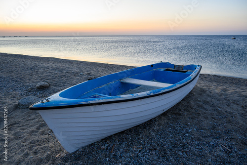 Small blue and white fishing boat resting on a sandy beach at dawn.