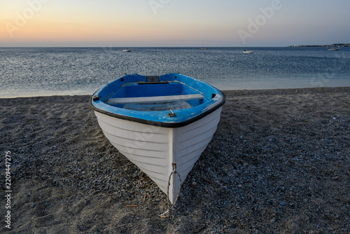 Small blue and white fishing boat resting on a sandy beach at dawn.